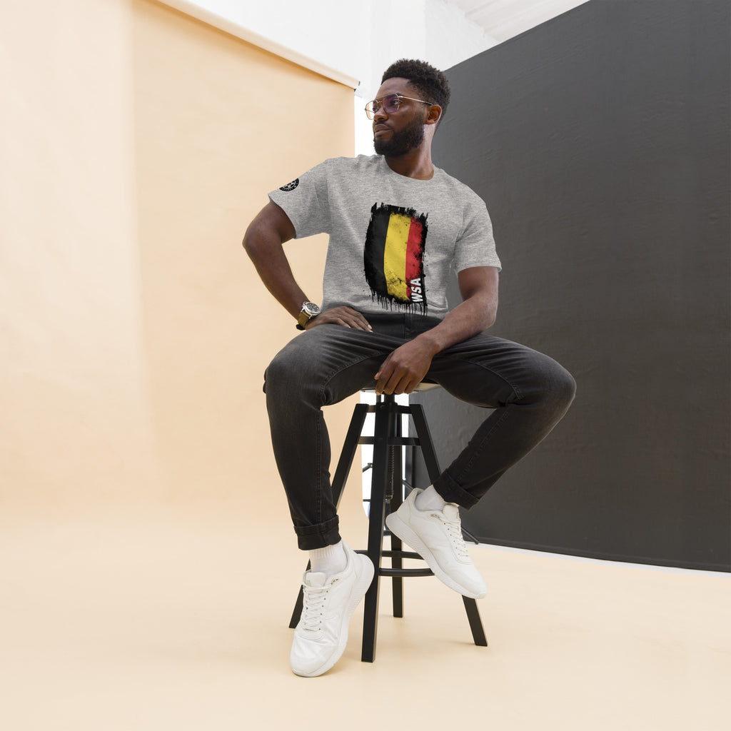 Man sitting on a stool wearing a gray t-shirt with a graphic design, black pants, and white sneakers.