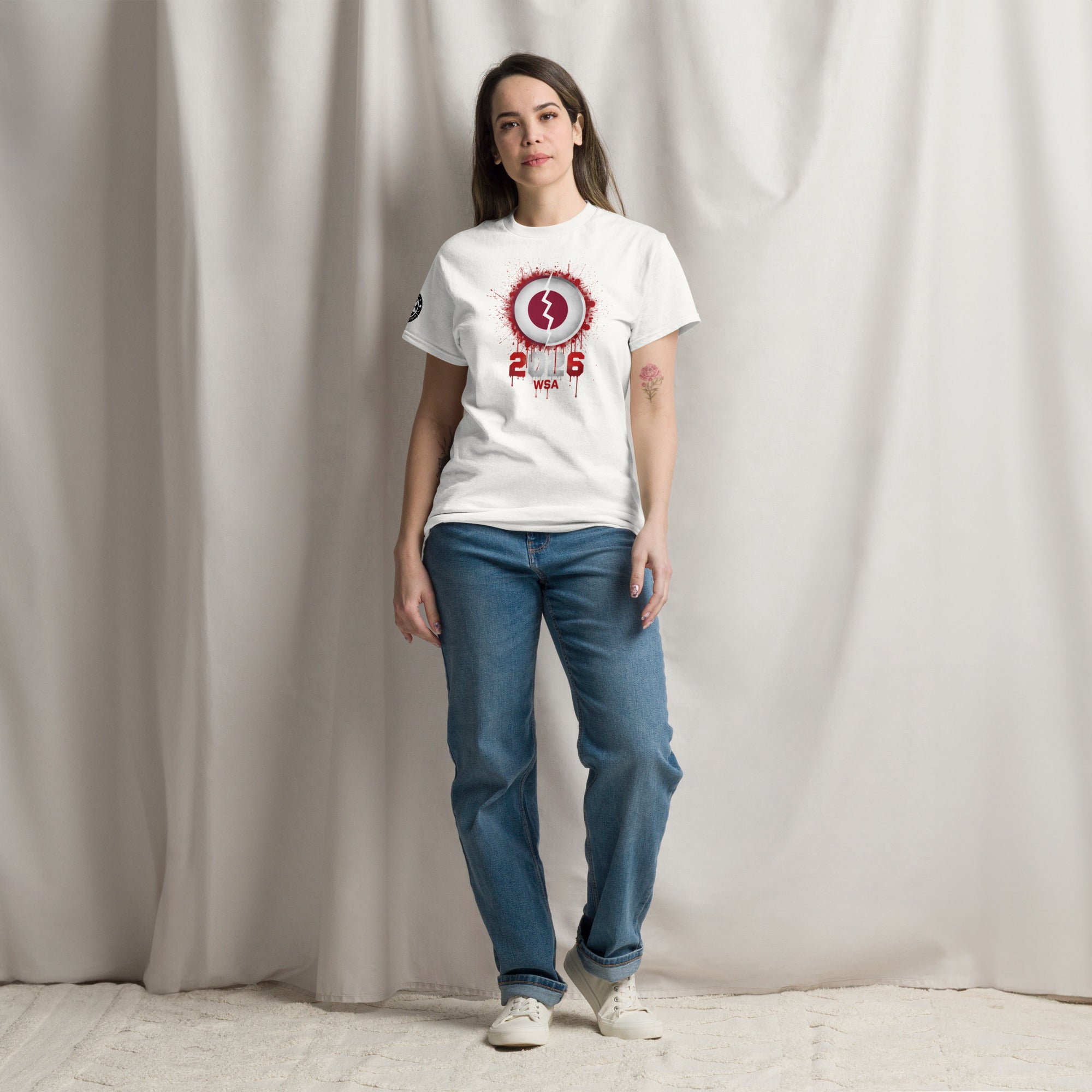 Woman wearing a white t-shirt with a red graphic design and blue jeans against a plain background