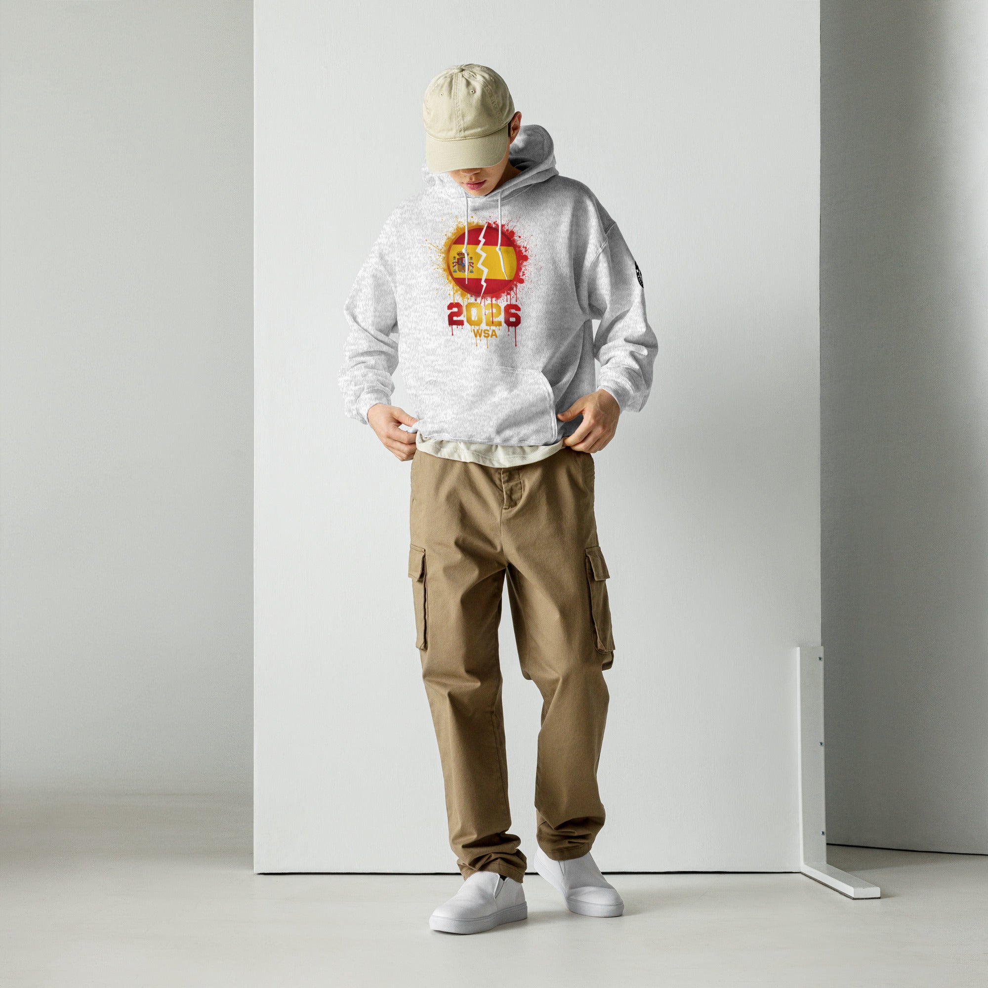 Person wearing a white hoodie with a logo and text, beige cap, brown cargo pants, and white shoes on a plain background.
