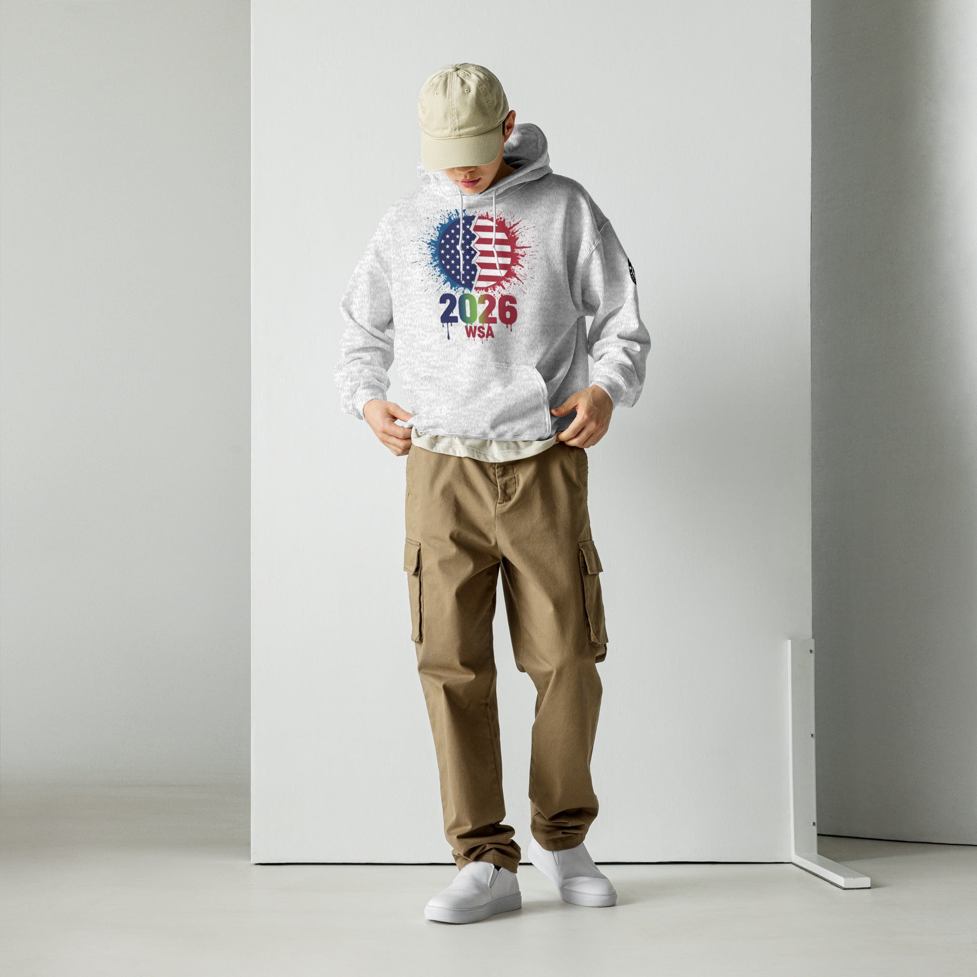 Person wearing a white hoodie with colorful design and text, beige cap, brown cargo pants, and white shoes on a plain background.