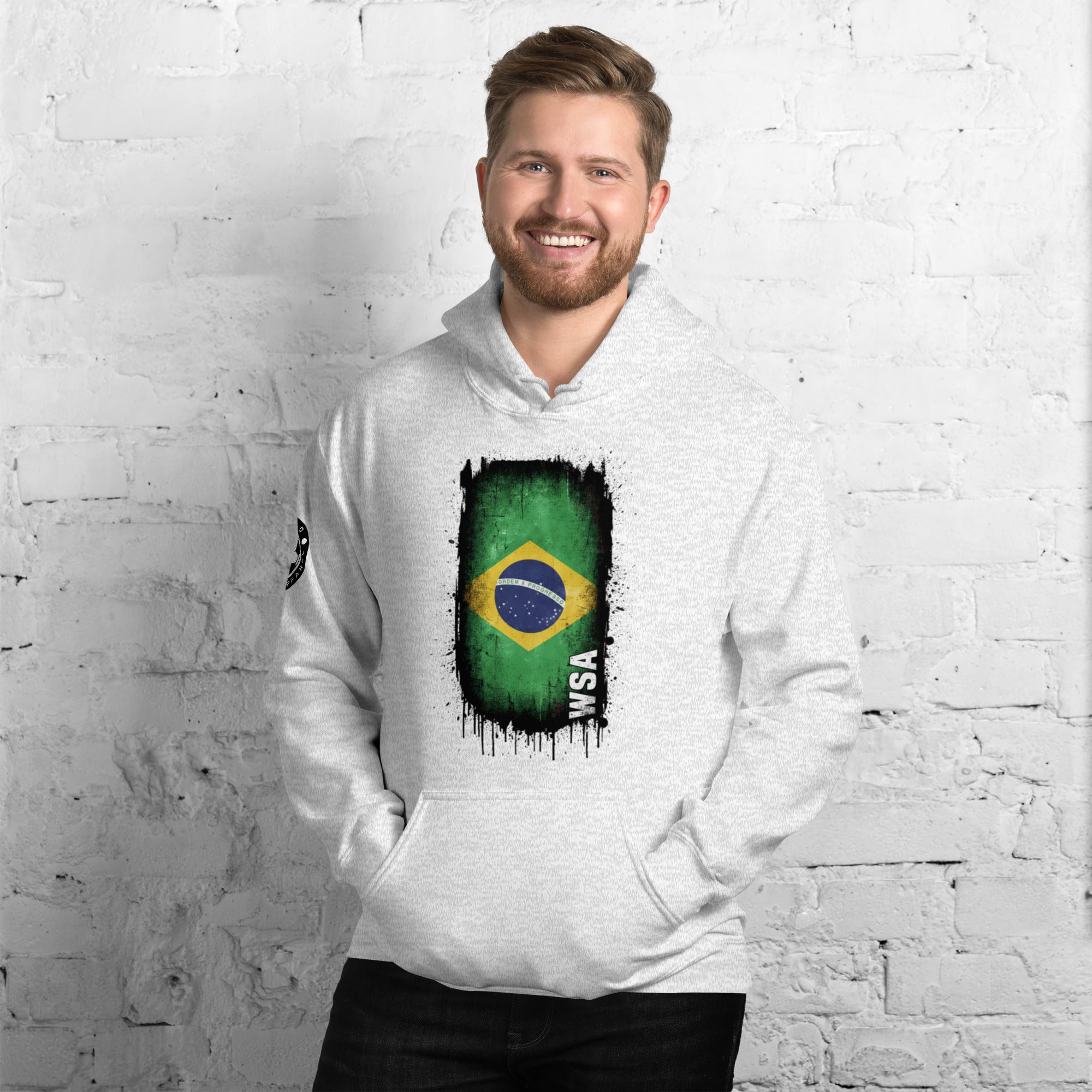 Man wearing a white hoodie with a Brazilian flag design against a white brick wall.