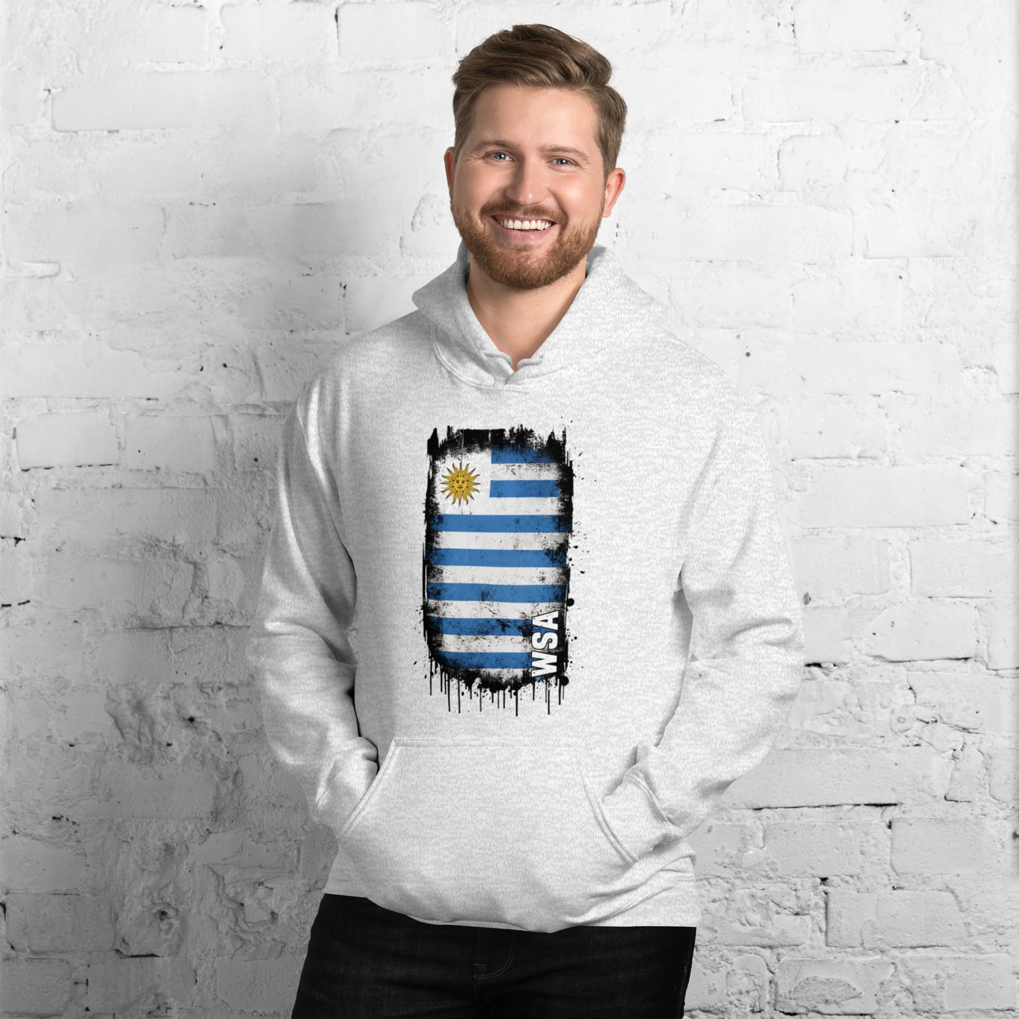 Man wearing a white hoodie with a flag design against a white brick wall.