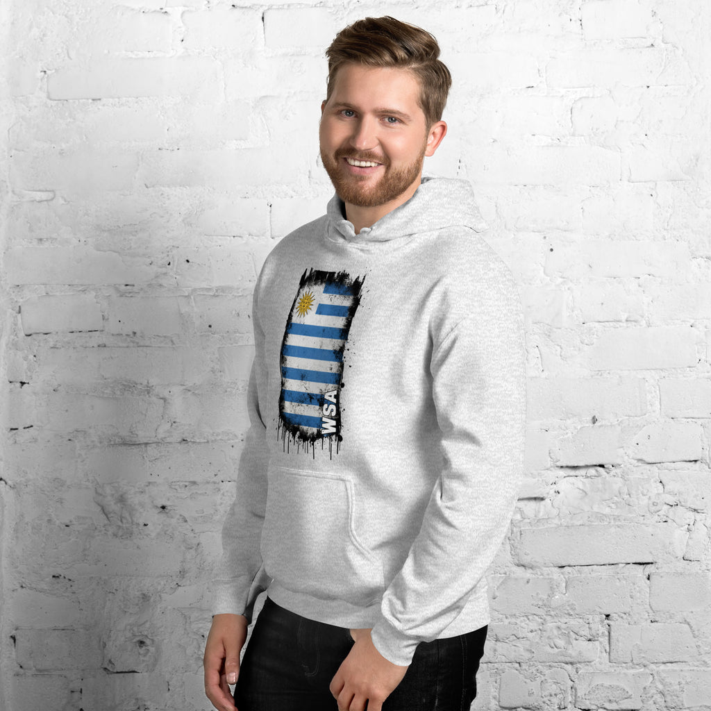 Man wearing a gray hoodie with a colorful graphic design against a white brick wall.