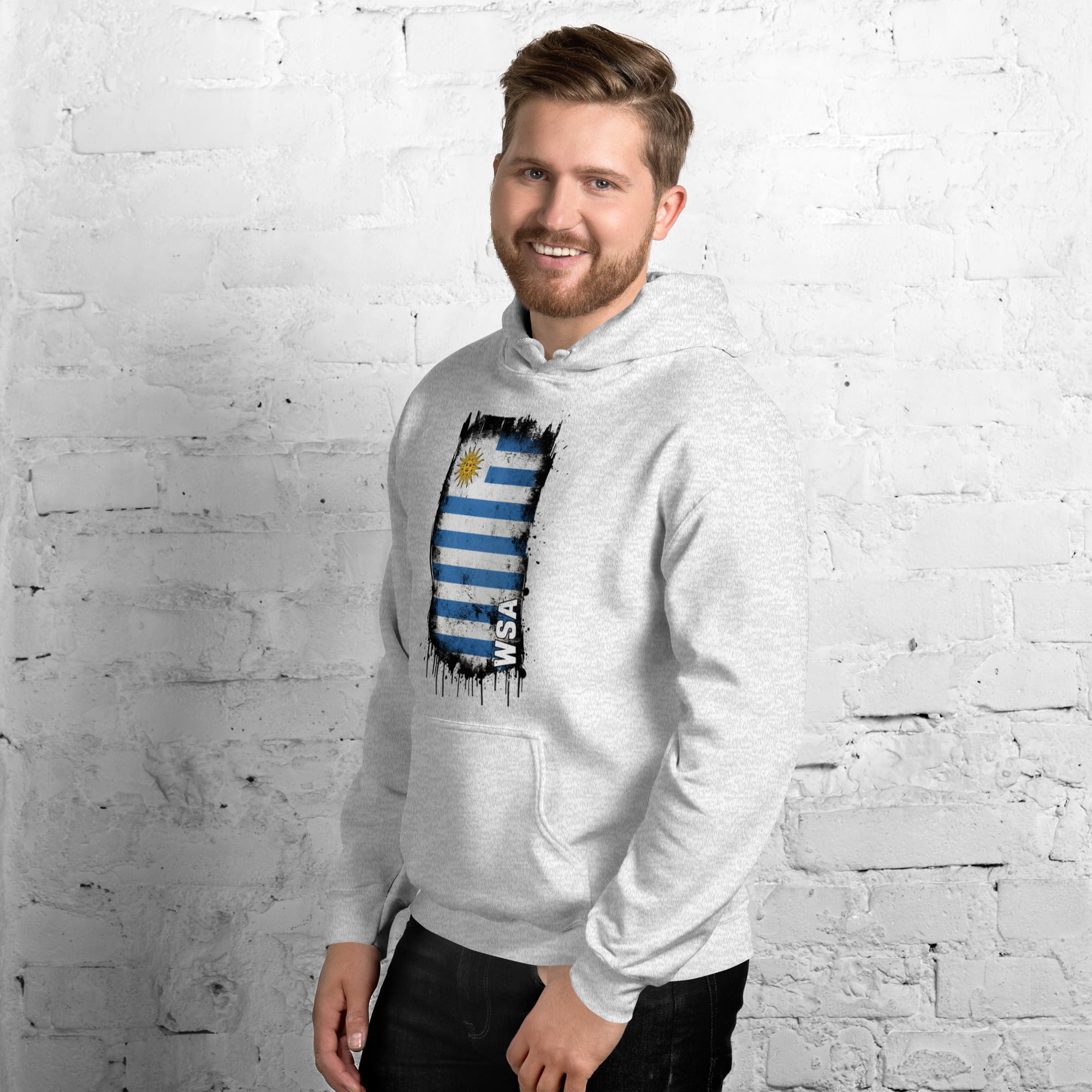 Man wearing a gray hoodie with a colorful graphic design against a white brick wall.