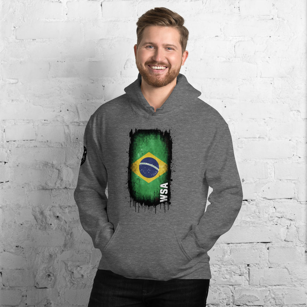 Man wearing a gray hoodie with a Brazilian flag design against a white brick wall.