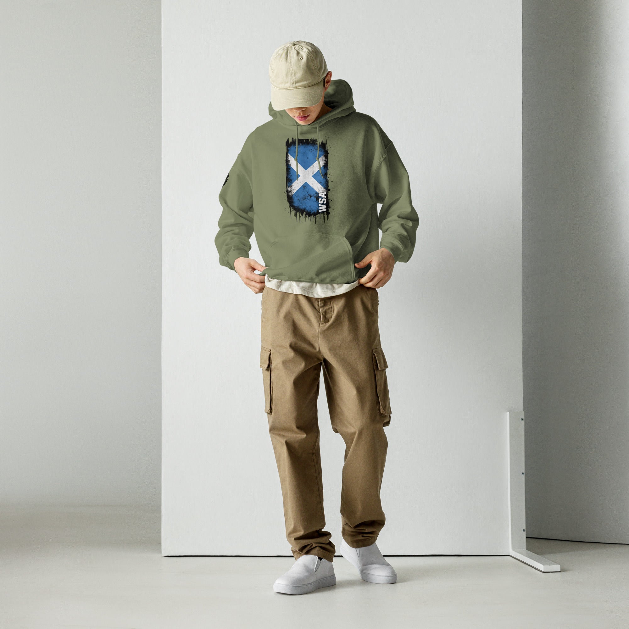 Person wearing a green hoodie with a design, brown cargo pants, and a beige cap against a white background