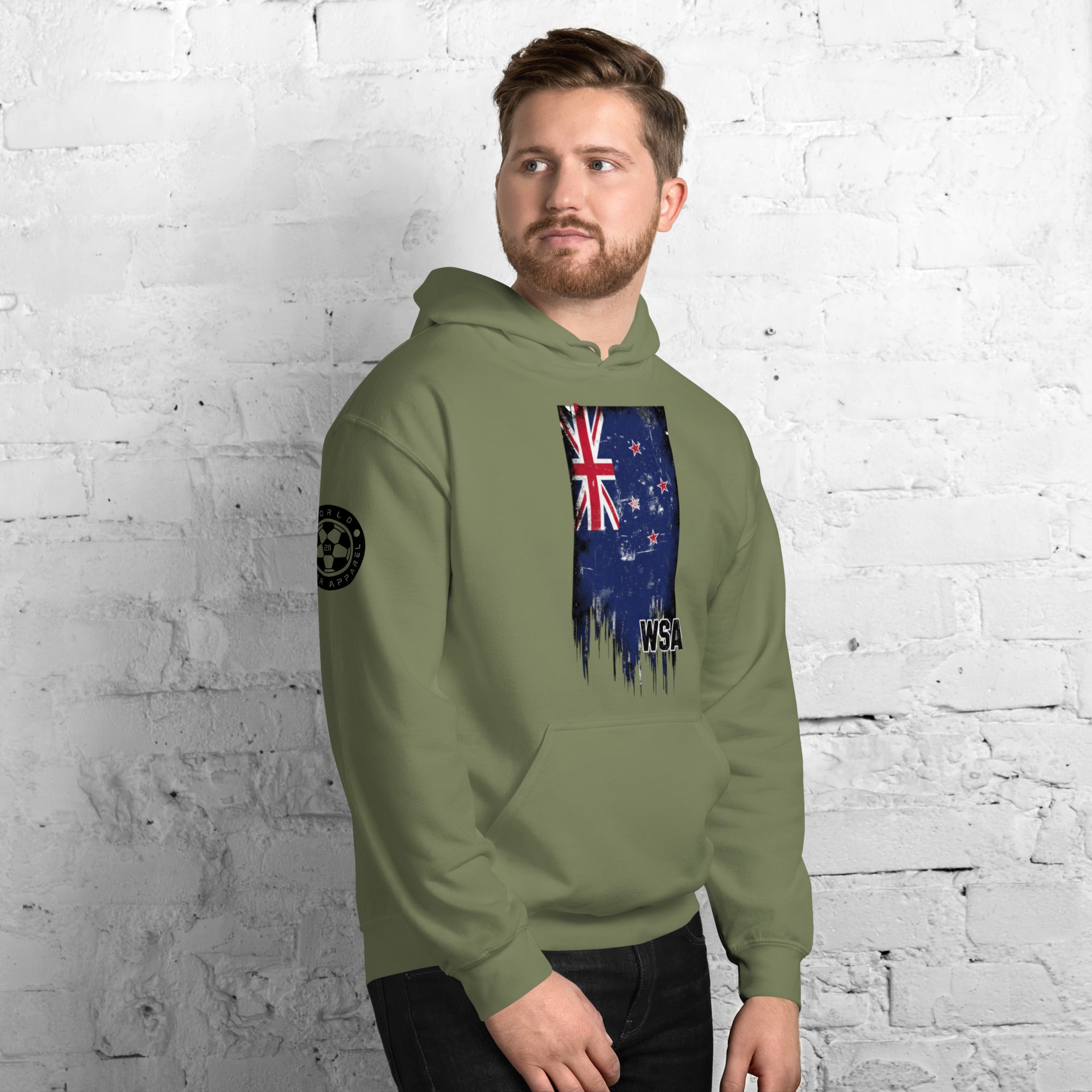 Man wearing a green hoodie with a flag design against a white brick wall.