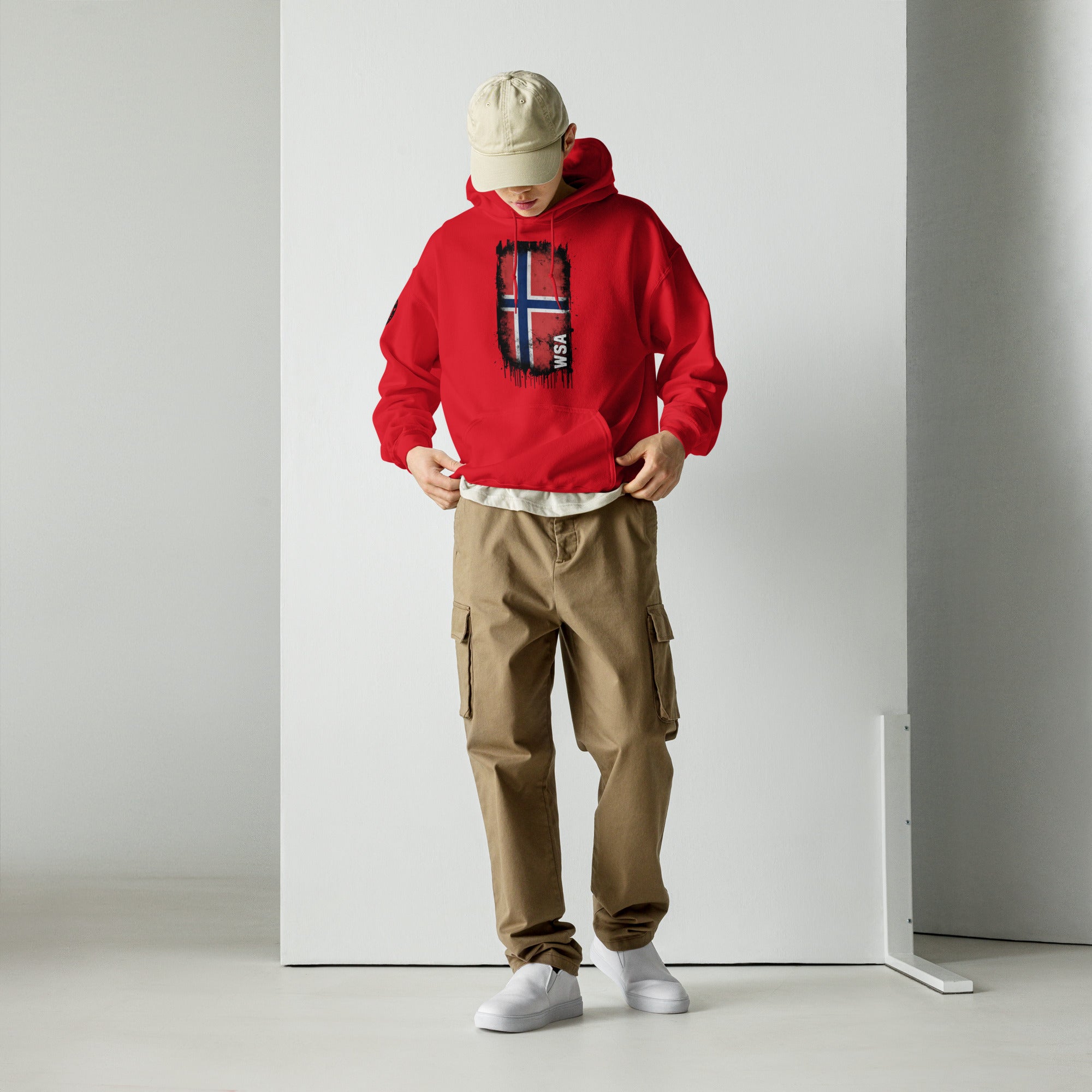Person wearing a red hoodie with a logo, beige cap, and brown cargo pants against a white background