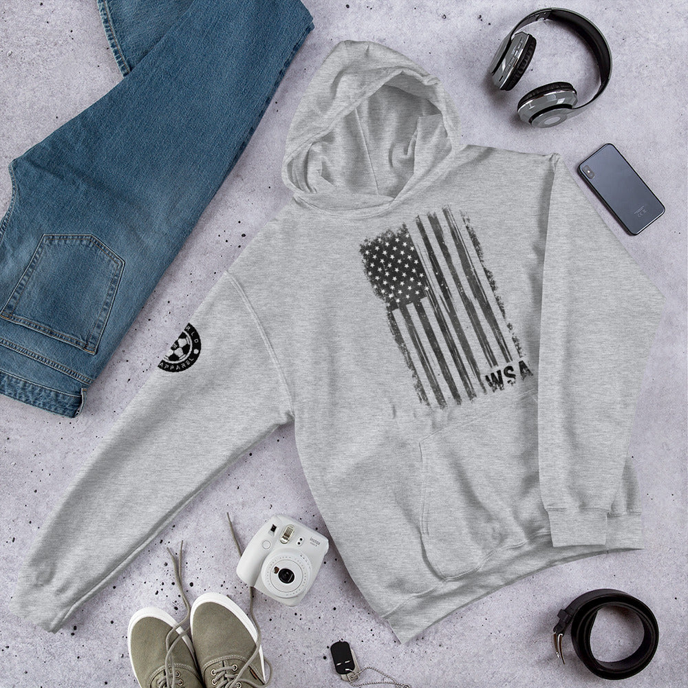 Gray hoodie with American flag design, jeans, shoes, camera, and accessories on a gray surface