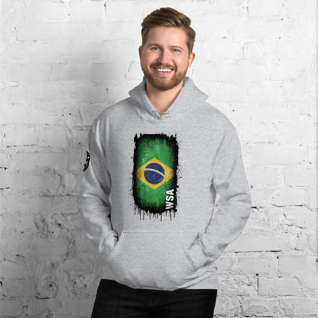 Man wearing a gray hoodie with a Brazilian flag design against a white brick wall.