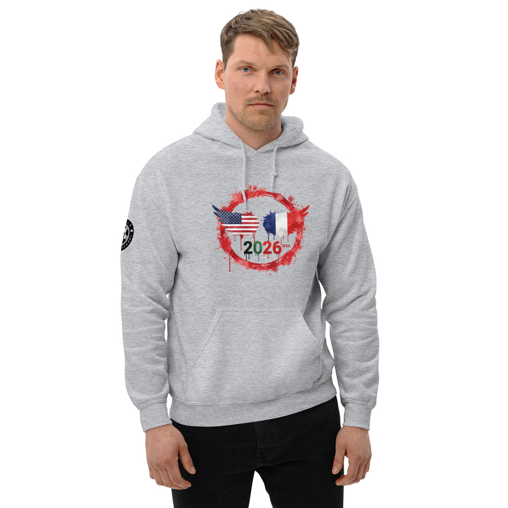 Man wearing a gray hoodie with a design featuring American and French flags and the number 2026 on a white background.