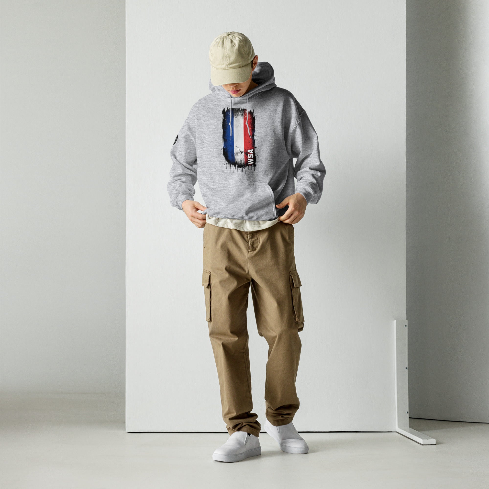 Person wearing a gray hoodie with a design and brown cargo pants standing against a white wall.