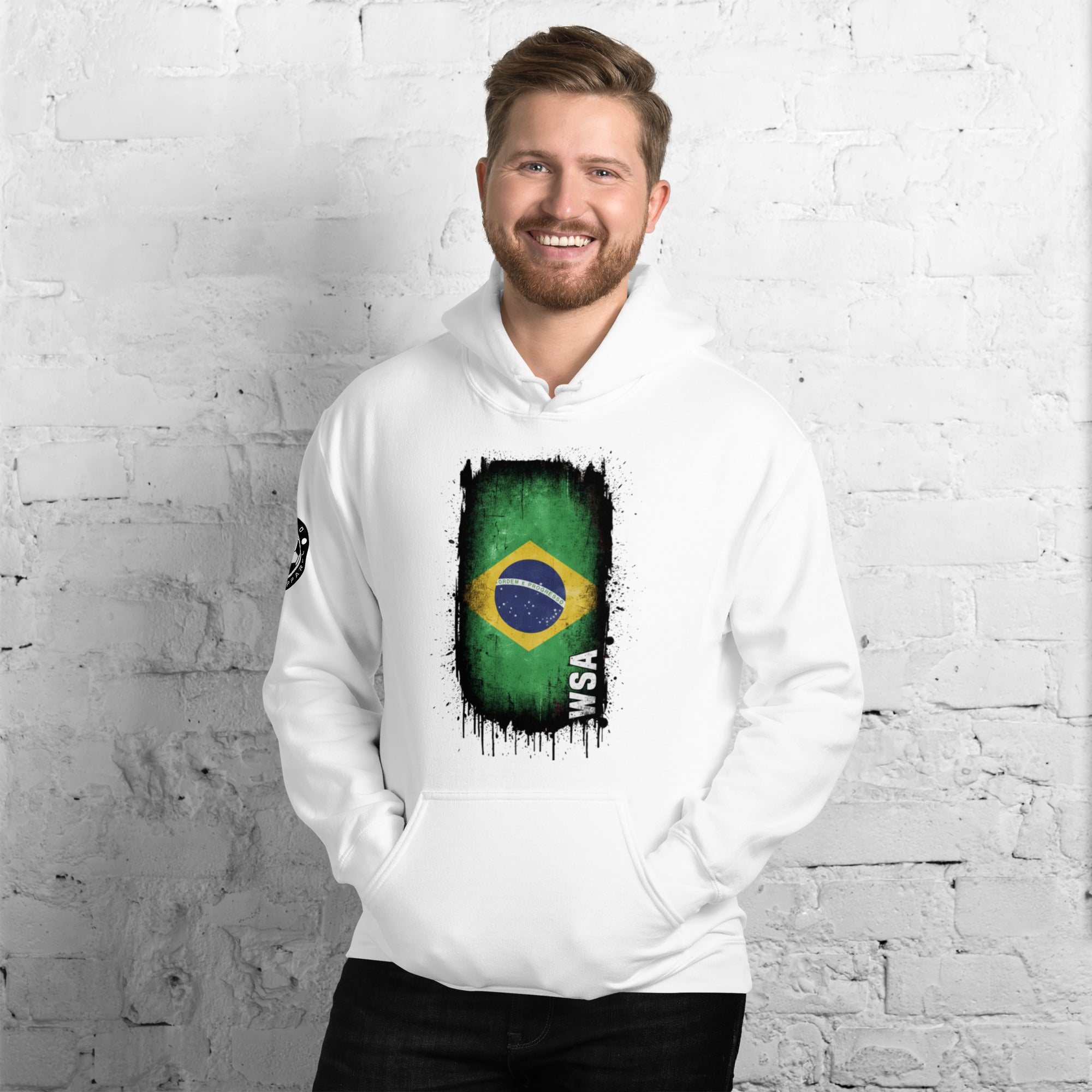 Man wearing a white hoodie with a Brazilian flag design against a white brick wall.