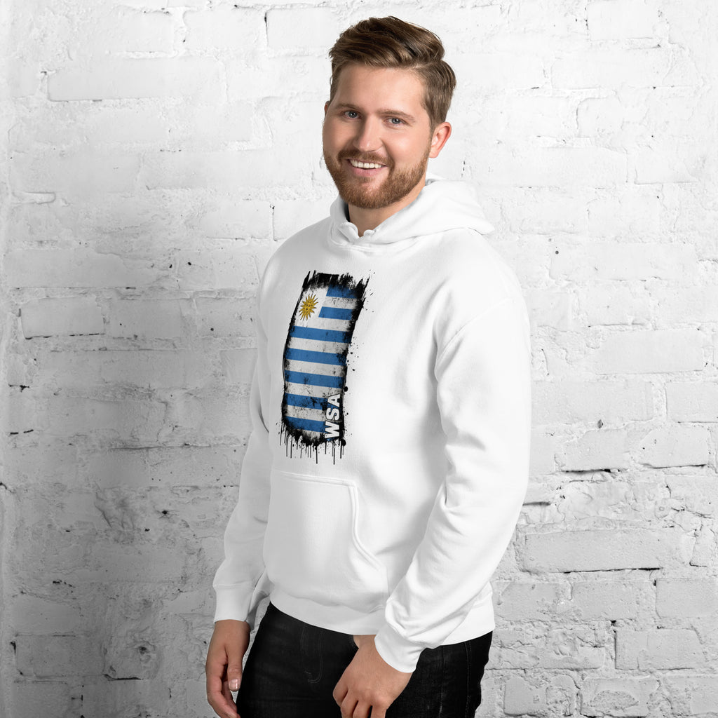 Man wearing a white hoodie with a flag design against a white brick wall.