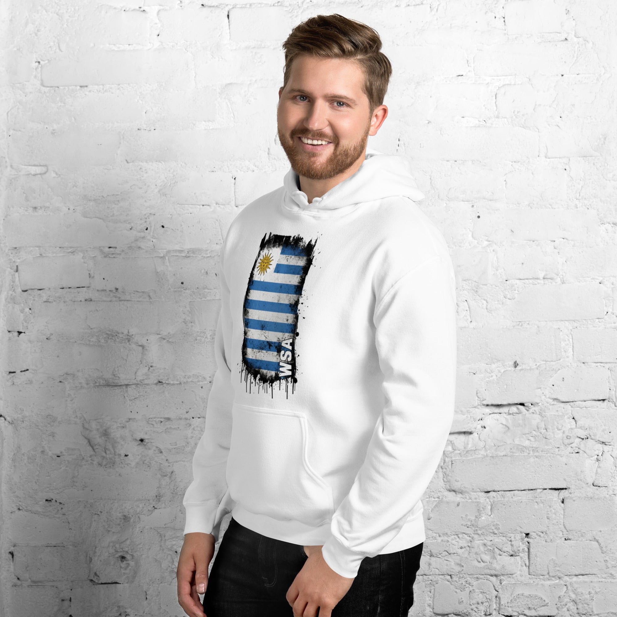 Man wearing a white hoodie with a flag design against a white brick wall.
