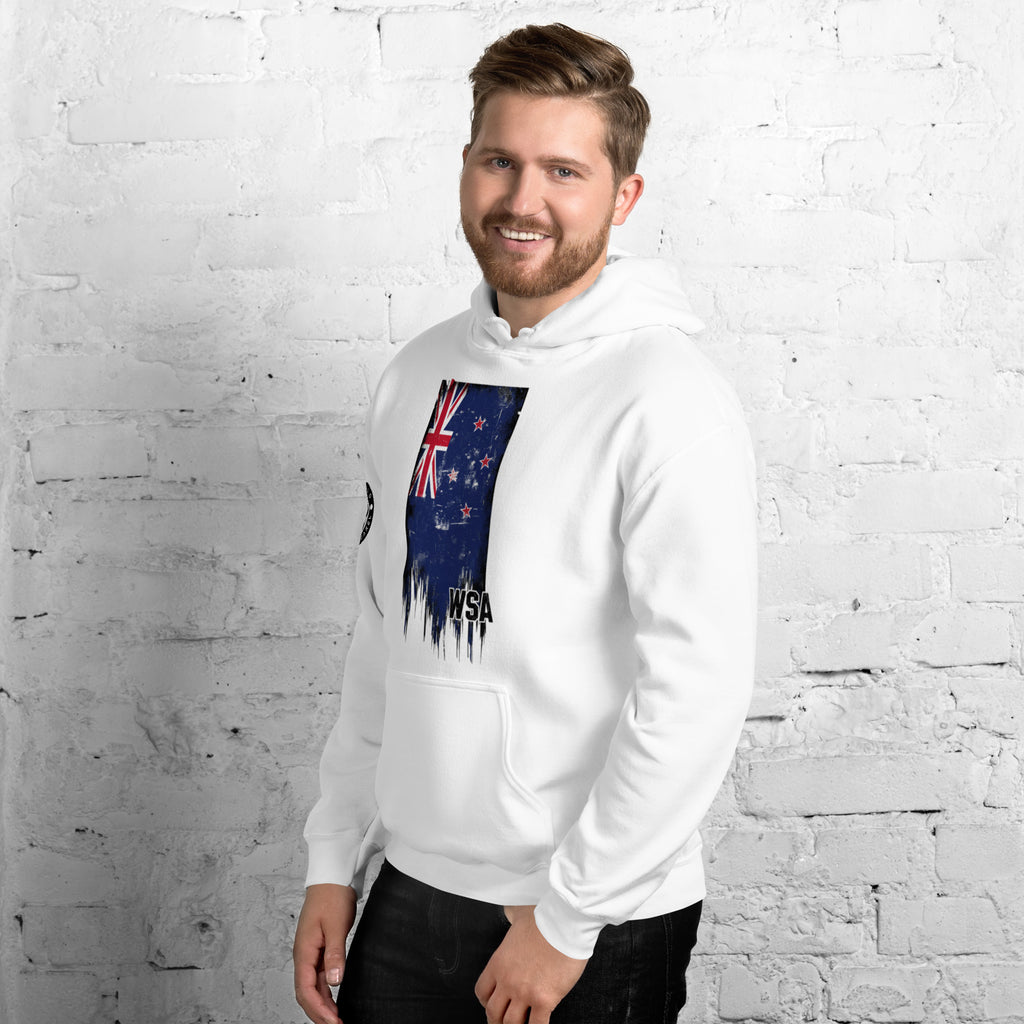 Man wearing a white hoodie with a flag design against a white brick wall.