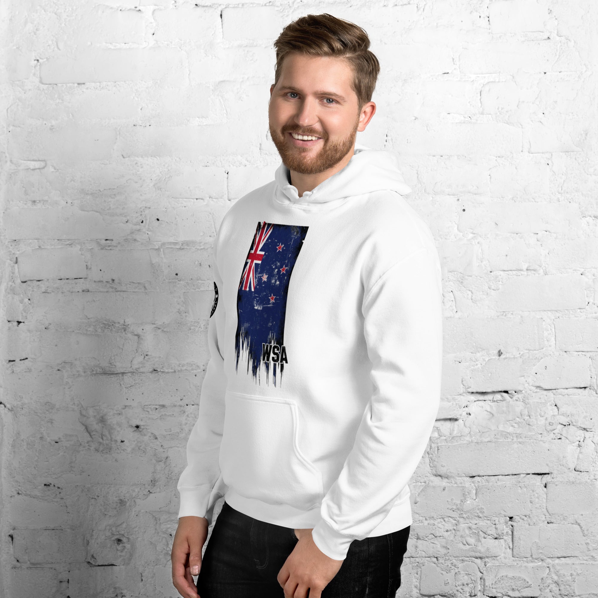 Man wearing a white hoodie with a flag design against a white brick wall.