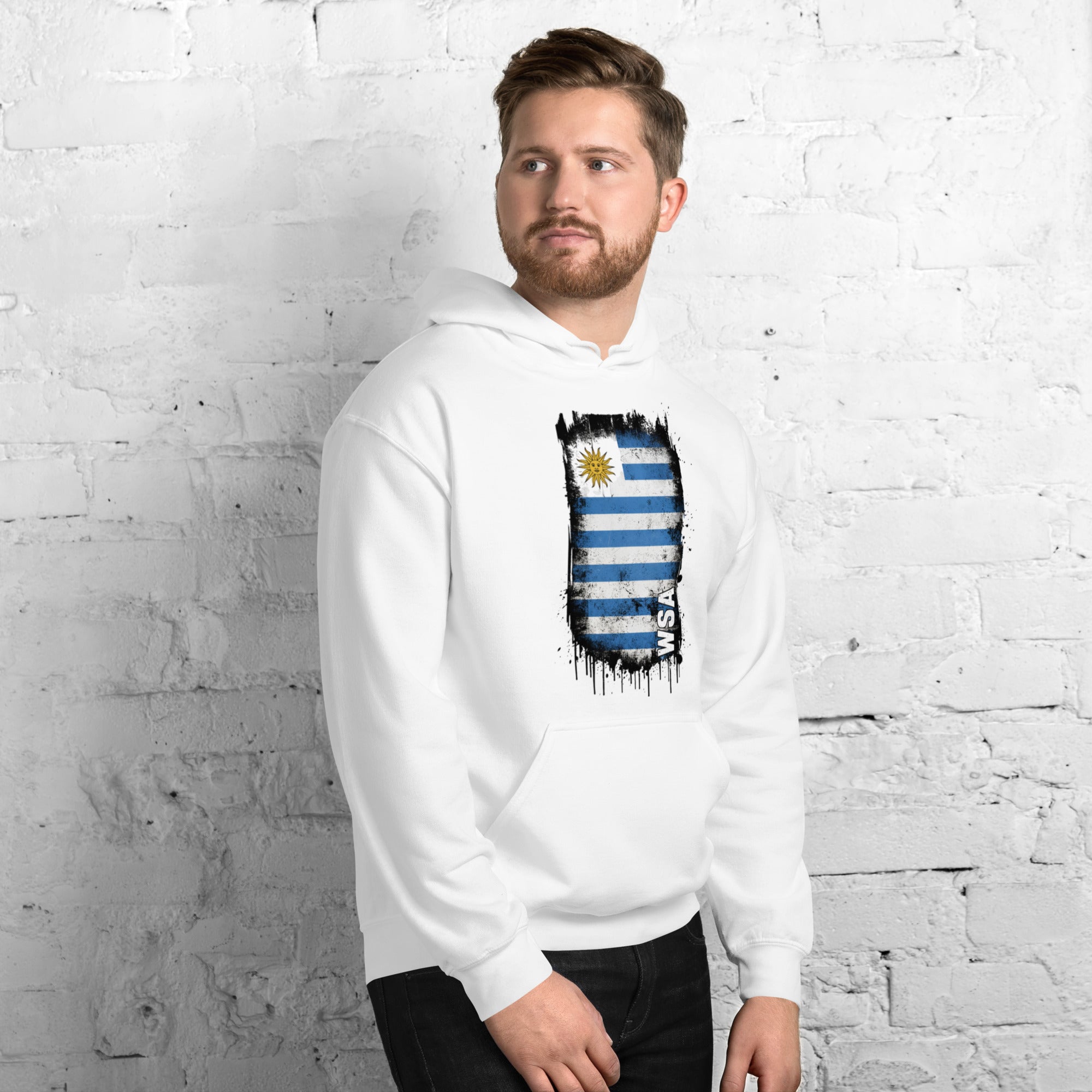 Man wearing a white hoodie with a flag design against a white brick wall.