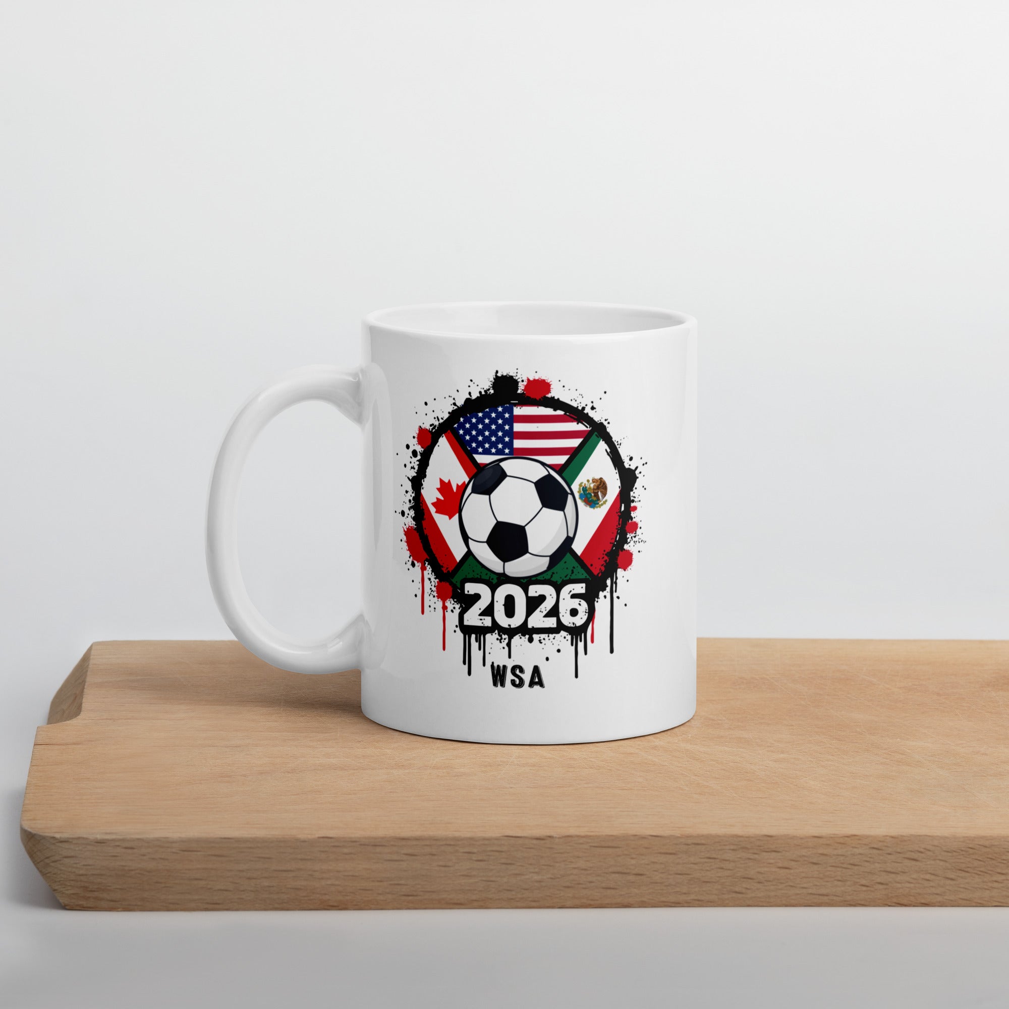 White mug with soccer ball design featuring flags and '2026 WSA' text on a wooden surface.