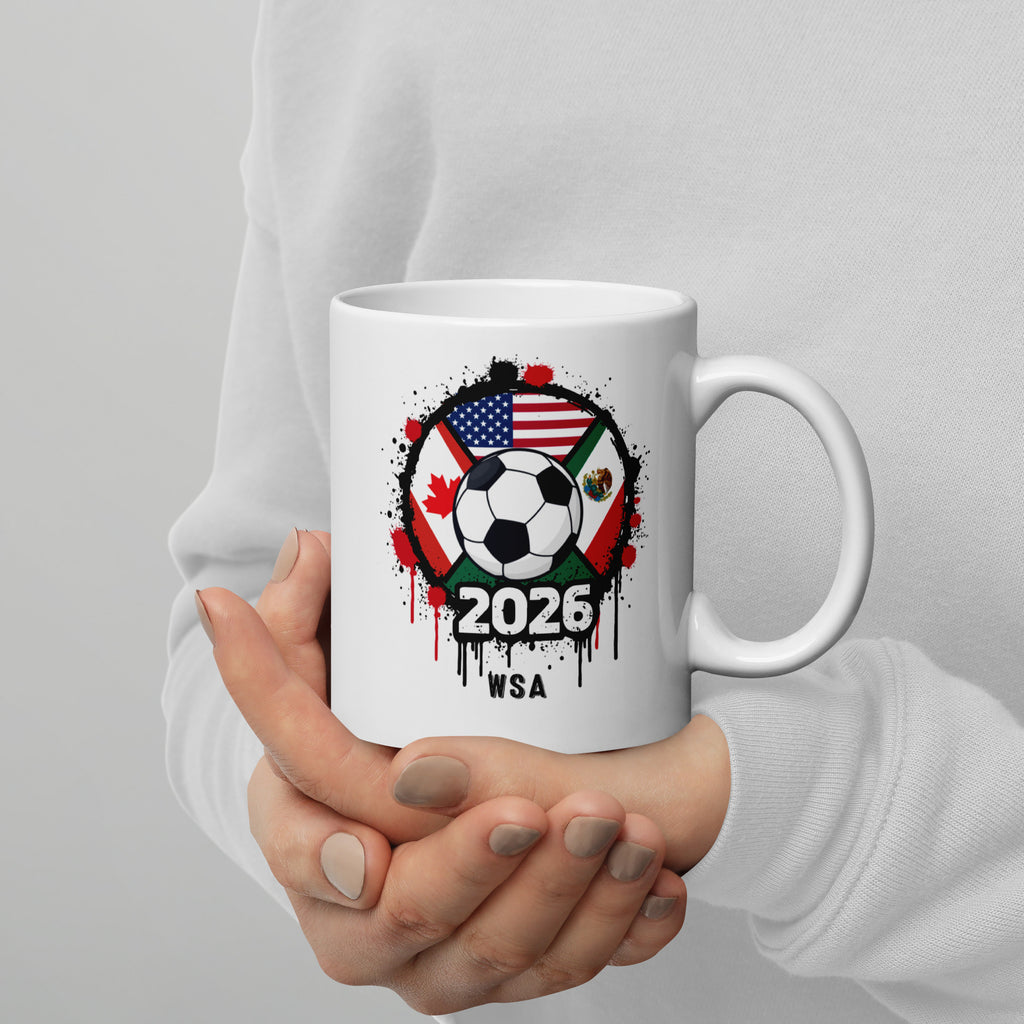 White mug with soccer ball and flags design held by a person against a gray background