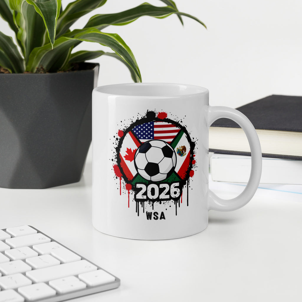 White mug with soccer ball and flags design on a desk with a plant and books in the background