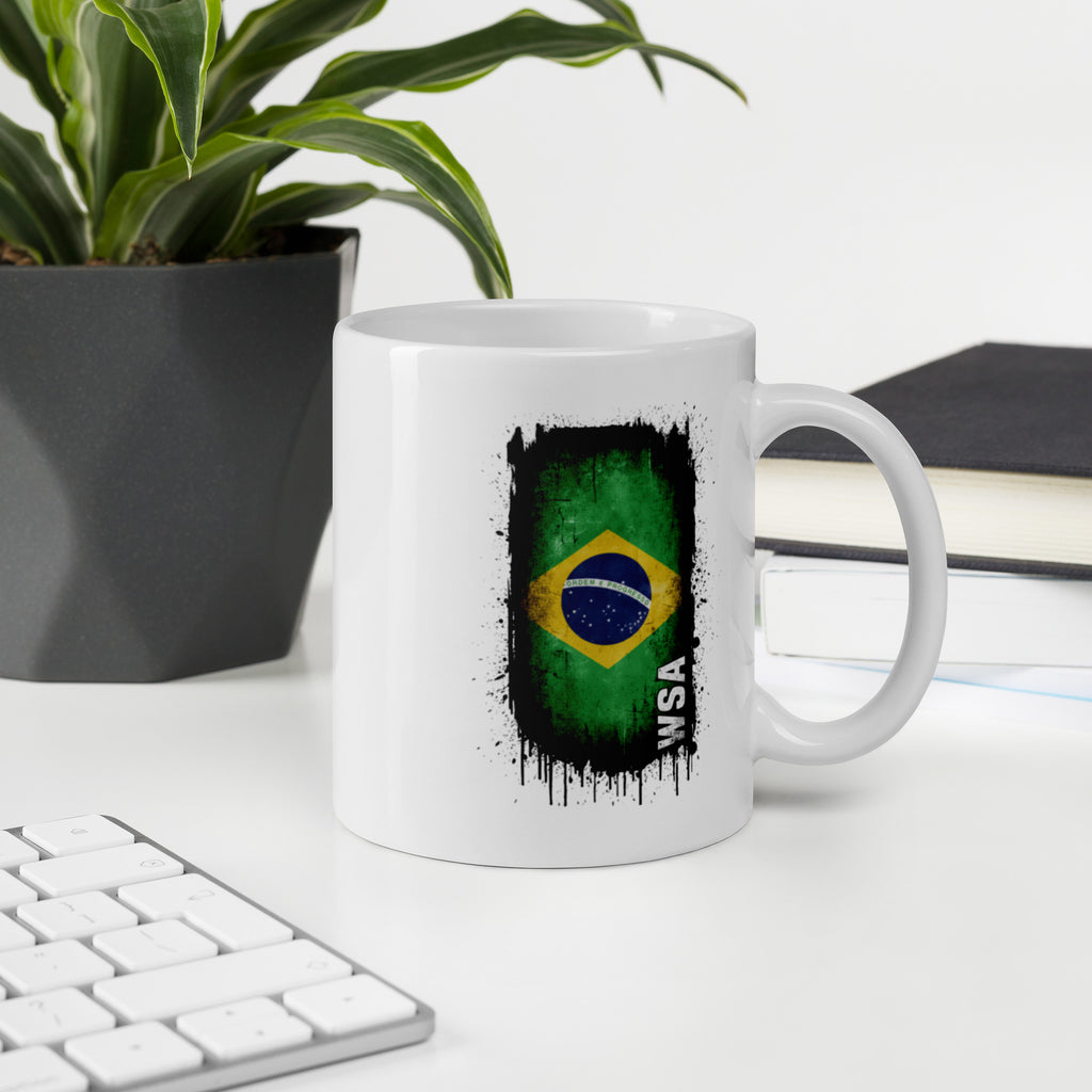 White mug with Brazilian flag design on a desk with a plant and books in the background
