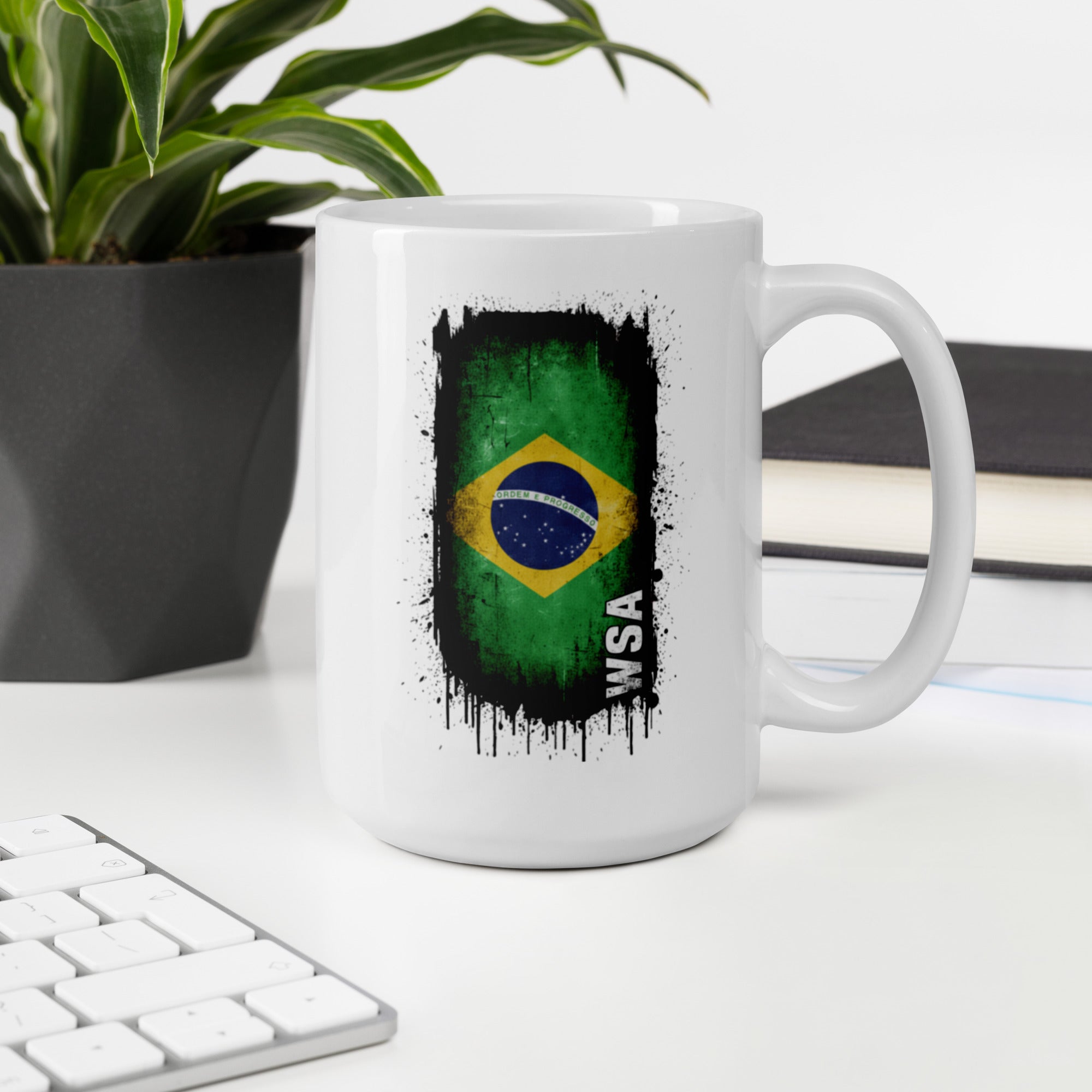 White mug with Brazilian flag design on a desk with a plant and books in the background