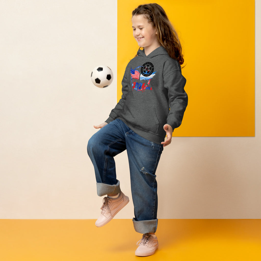 Child in a gray hoodie with a graphic design, kicking a soccer ball against a yellow and beige background