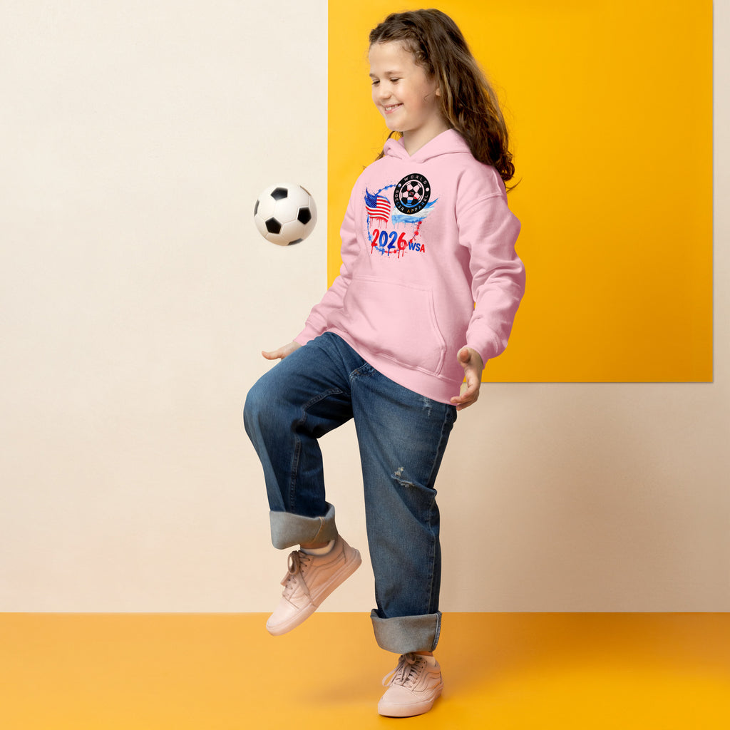 Child wearing a pink hoodie with sports-themed design, kicking a soccer ball against a yellow and beige background.